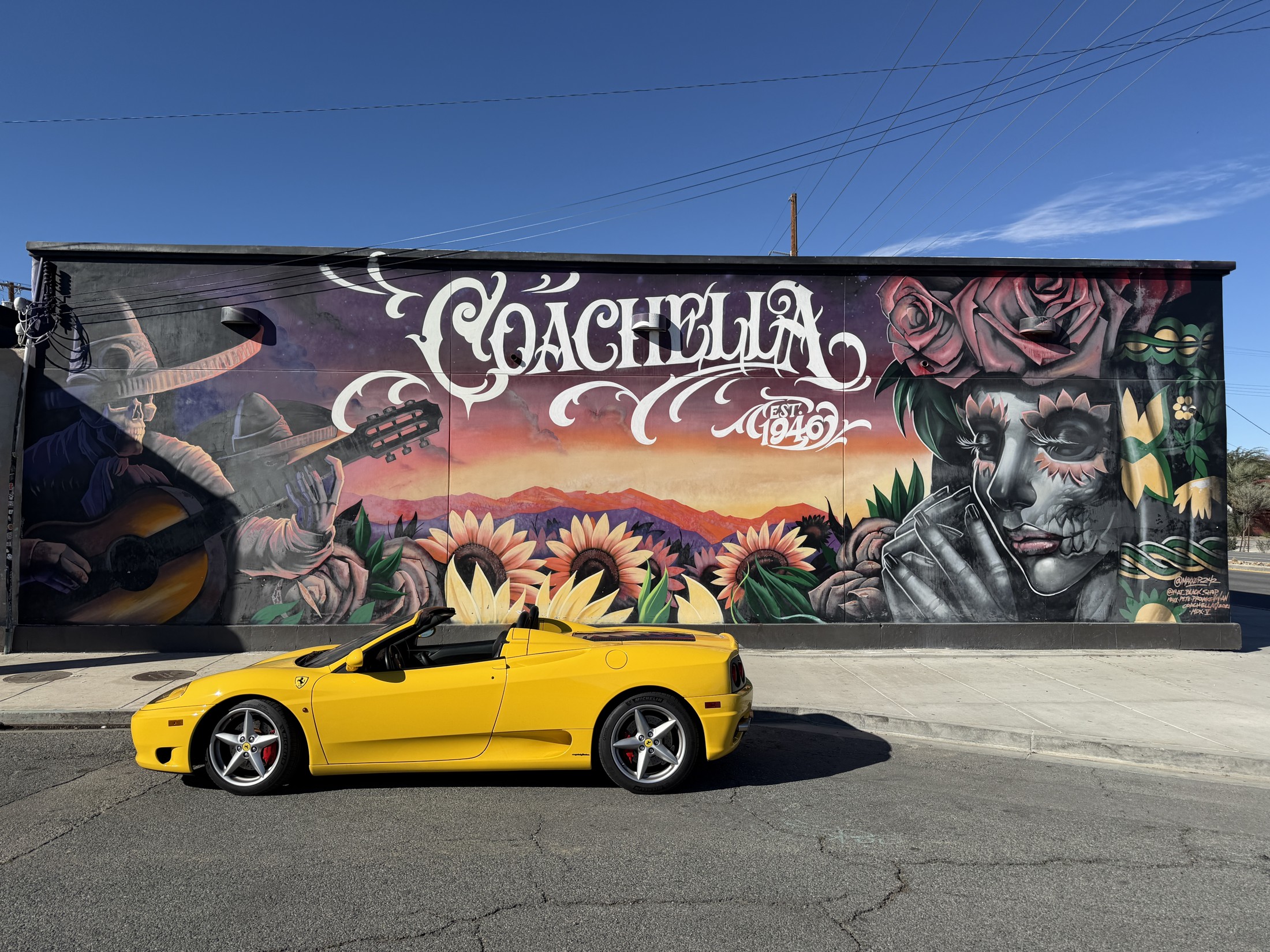 Yellow Ferrari 360 Spider parked in front of a colourful Coachella mural, with no people in the photograph