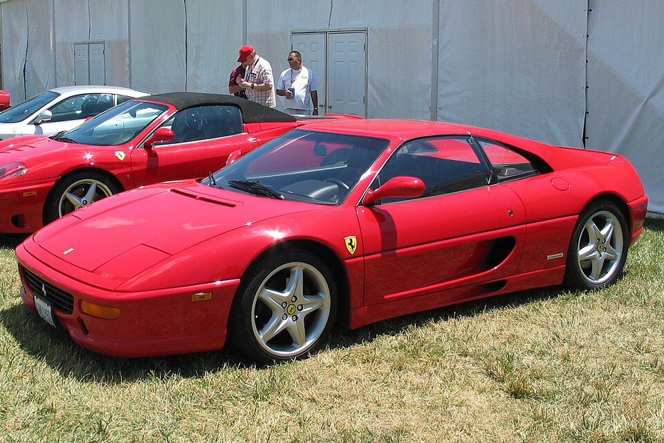 Red Ferrari F355 Berlinetta seen from a front three-quarter angle, showing its smooth body and sculpted side air intake.